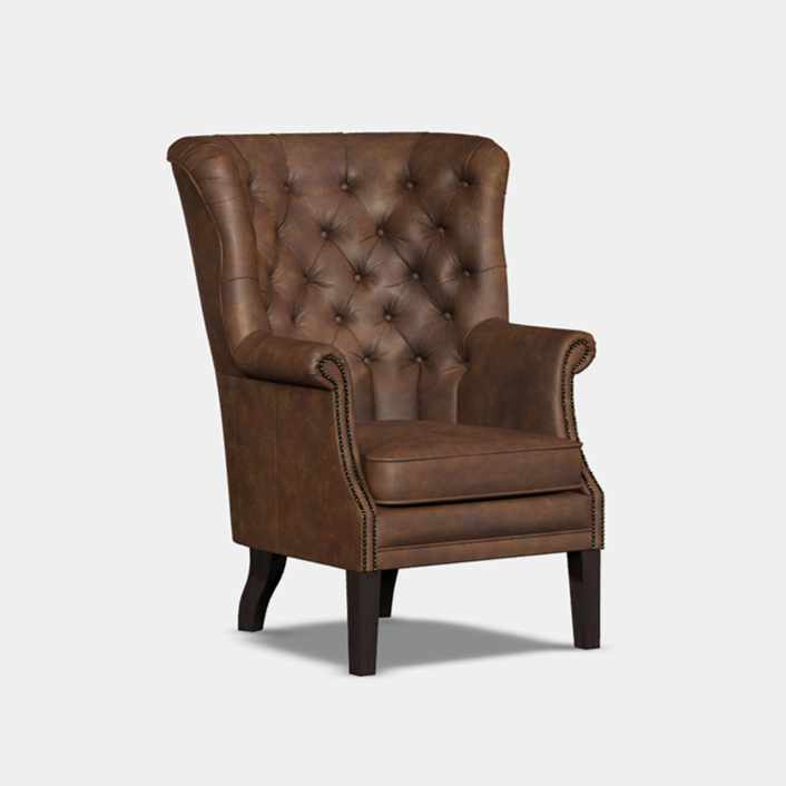 A traditional brown wing chair with deep buttoning and scroll arms, featuring hand stud detailing on a white background.