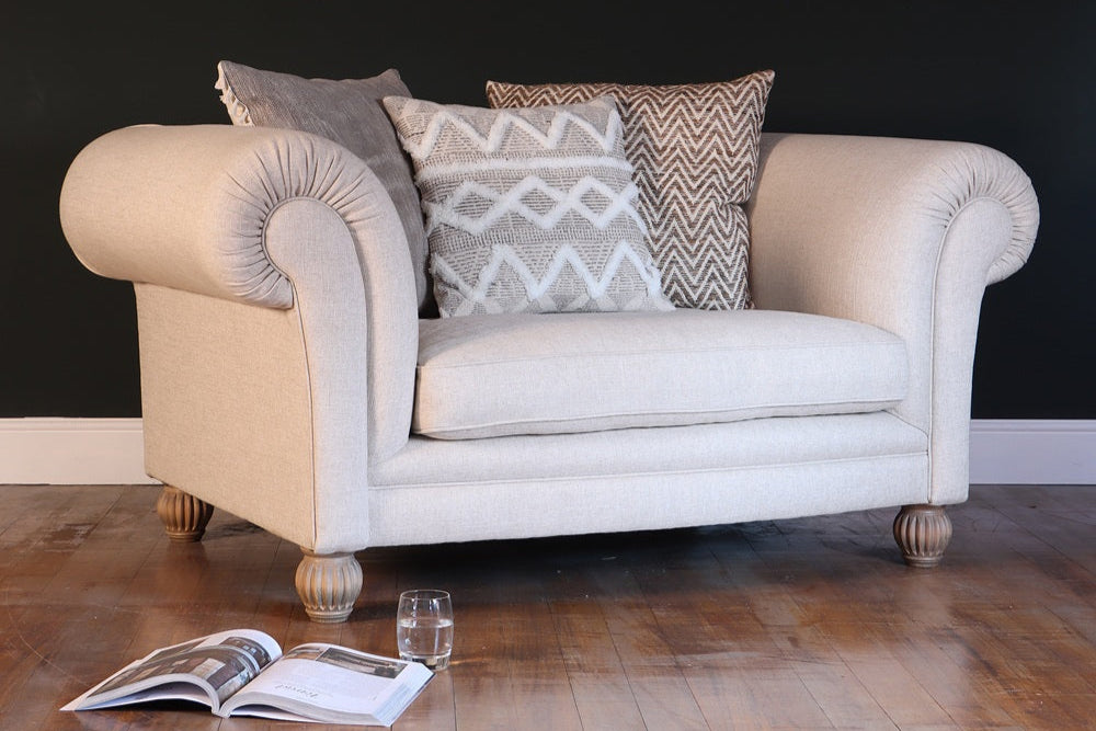 Beige armchair with patterned cushions in a room with a dark wall and wooden floor.
