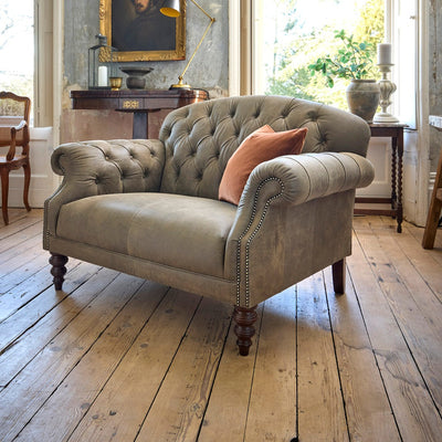 Gray tufted sofa with a pink pillow in a room with wooden floors and large windows.
