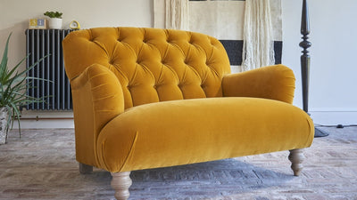 Yellow velvet sofa in a living room with a patterned wall hanging and lamp.
