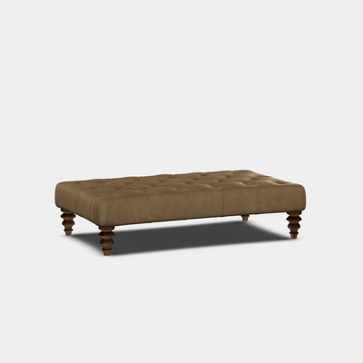 A brown, buttoned footstool with curved sides and wooden legs, set against a white background.
