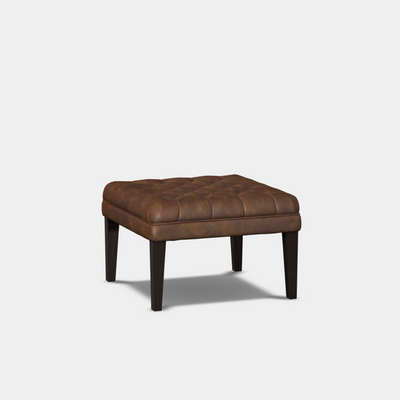 A brown upholstered square stool with deep button design and leather piping, set against a white background.