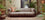 Decorative living room with a gray sofa, plants, and a framed picture on a brick wall.