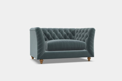 A contemporary blue chesterfield sofa with deep button detail and hardwood feet, designed for elegant lounging in living spaces.