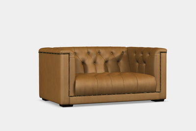 A brown leather loveseat sofa with tufted backrest and slender arms with hand studded detail.